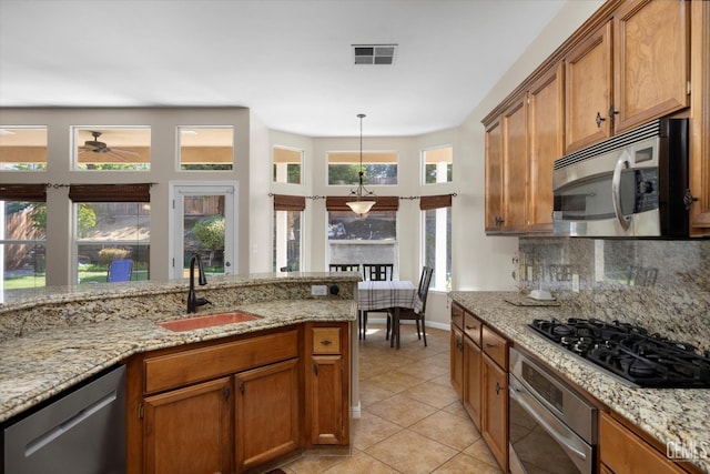 kitchen with light tile patterned flooring, ceiling fan, a sink, brown cabinetry, and stainless steel appliances