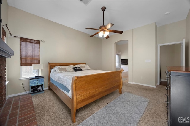 carpeted bedroom with baseboards, arched walkways, a brick fireplace, and a ceiling fan