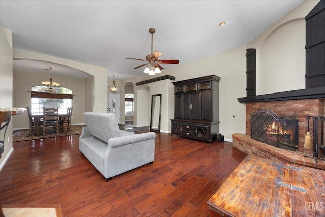 living room featuring arched walkways, ceiling fan with notable chandelier, dark wood-type flooring, and a fireplace