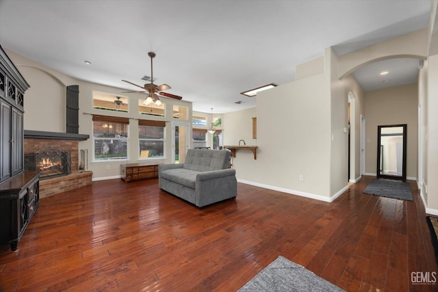 living room with a ceiling fan, arched walkways, a brick fireplace, baseboards, and wood-type flooring