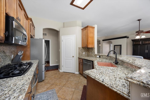 kitchen with decorative backsplash, a sink, ceiling fan, arched walkways, and appliances with stainless steel finishes
