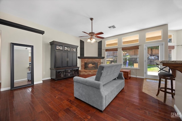 living room with ceiling fan, visible vents, a fireplace, baseboards, and dark wood-style floors