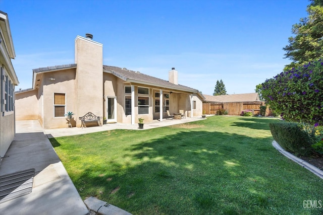 rear view of property with fence, stucco siding, a chimney, a lawn, and a patio