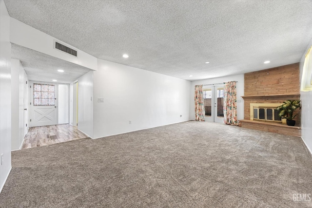 unfurnished living room with visible vents, a large fireplace, carpet, and french doors