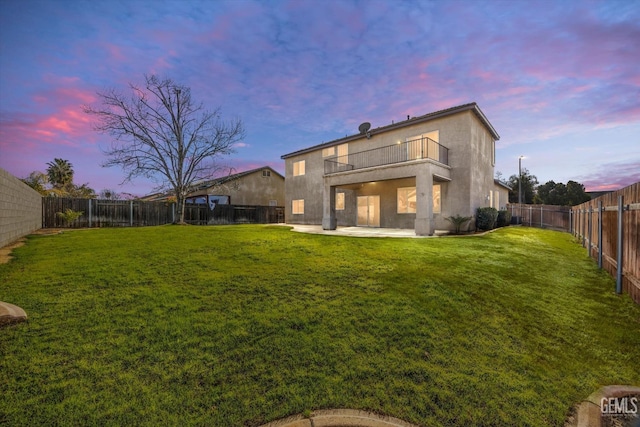 back house at dusk featuring a yard, a balcony, and a patio area