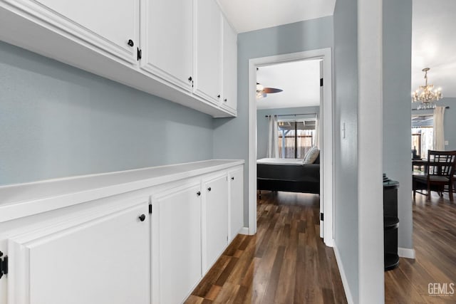 corridor with baseboards, dark wood-type flooring, and a chandelier