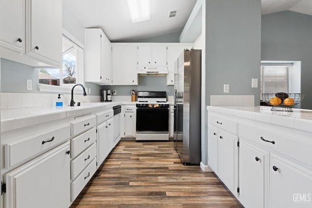 kitchen featuring under cabinet range hood, lofted ceiling, range with gas stovetop, stainless steel fridge, and a sink