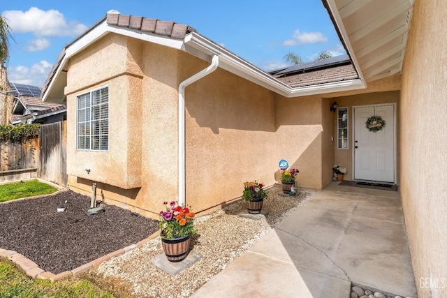 property entrance featuring stucco siding, solar panels, and fence