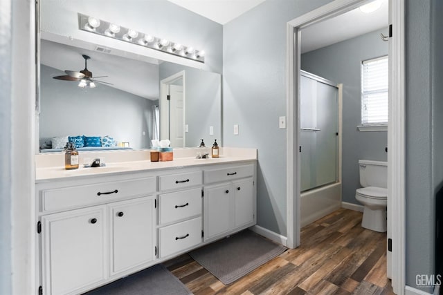 full bath featuring toilet, wood finished floors, double vanity, baseboards, and ceiling fan