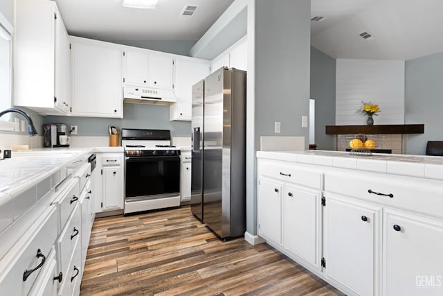 kitchen with visible vents, under cabinet range hood, a sink, stainless steel fridge, and gas range