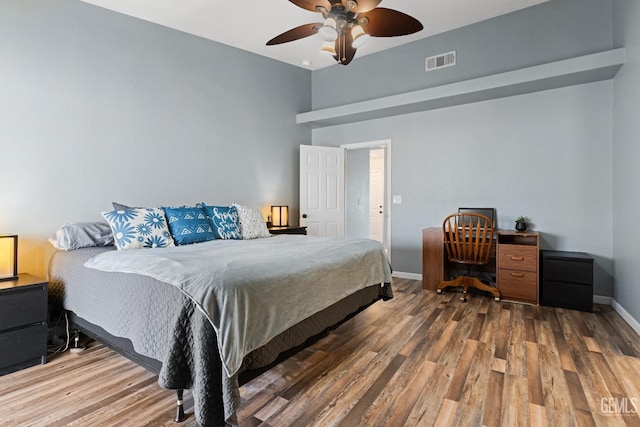 bedroom with a ceiling fan, wood finished floors, visible vents, and baseboards