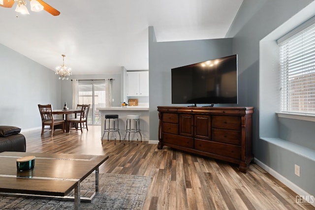 living room featuring ceiling fan with notable chandelier, vaulted ceiling, wood finished floors, and baseboards