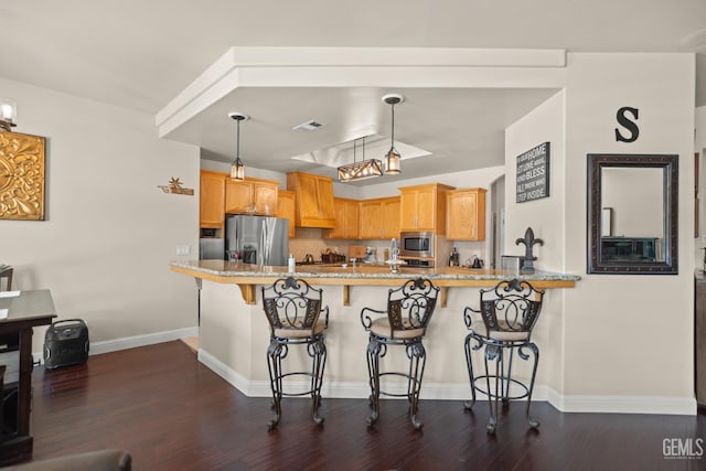 kitchen featuring pendant lighting, a breakfast bar, stainless steel appliances, dark hardwood / wood-style flooring, and kitchen peninsula