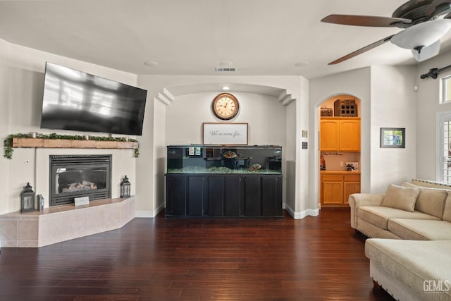 living room featuring dark hardwood / wood-style flooring, a tile fireplace, and ceiling fan