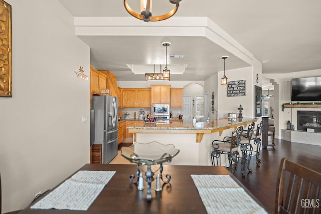 kitchen with a breakfast bar, appliances with stainless steel finishes, hanging light fixtures, dark hardwood / wood-style floors, and light stone countertops