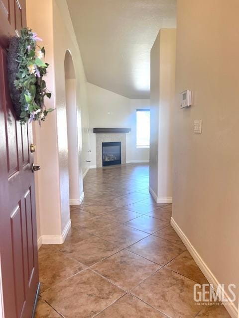 11422 Pacific Harbor Ave, Bakersfield, CA 93312 - unfurnished living room featuring light tile patterned floors, vaulted ceiling, a glass covered fireplace, and arched walkways