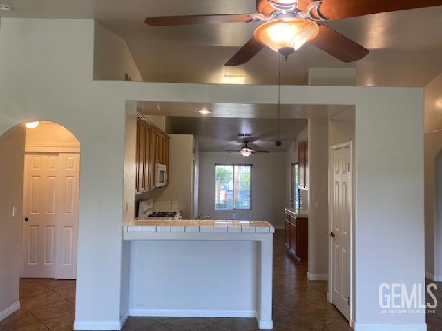 11422 Pacific Harbor Ave, Bakersfield, CA 93312 - kitchen with ceiling fan, tile countertops, a peninsula, arched walkways, and white microwave