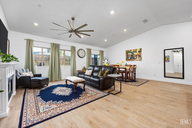 living area featuring light wood finished floors, visible vents, a ceiling fan, a glass covered fireplace, and vaulted ceiling