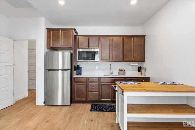 kitchen with wood counters, a sink, stainless steel appliances, light wood-type flooring, and backsplash