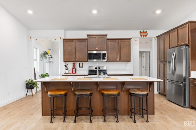 kitchen with appliances with stainless steel finishes, light countertops, a sink, and a center island with sink