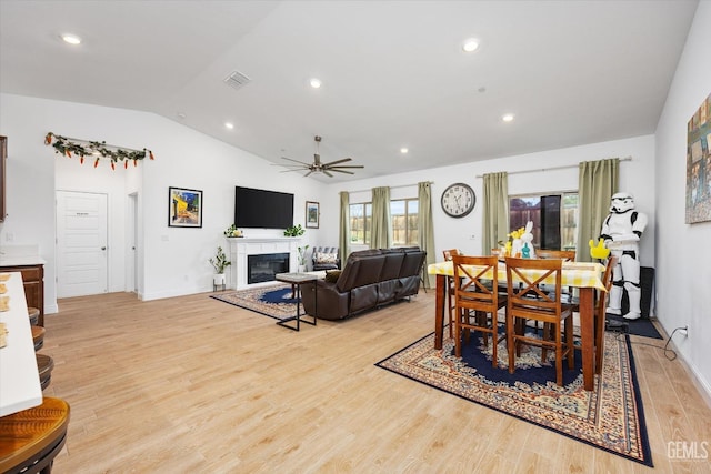 dining space with plenty of natural light, visible vents, a glass covered fireplace, lofted ceiling, and light wood-type flooring