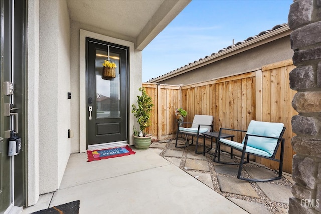 view of exterior entry featuring fence, a patio, and stucco siding