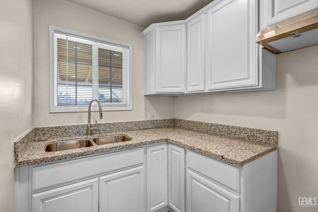 kitchen with light stone counters, sink, and white cabinets