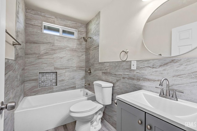 full bathroom featuring tiled shower / bath, tile walls, vanity, and toilet