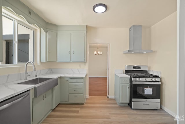 kitchen with light wood-type flooring, light stone counters, stainless steel appliances, sink, and wall chimney range hood