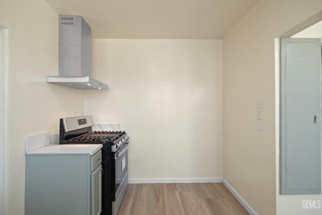 kitchen featuring wall chimney exhaust hood, gray cabinetry, gas range, light hardwood / wood-style flooring, and washer / dryer