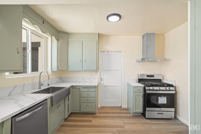 kitchen featuring appliances with stainless steel finishes, light wood-type flooring, light stone counters, wall chimney exhaust hood, and sink