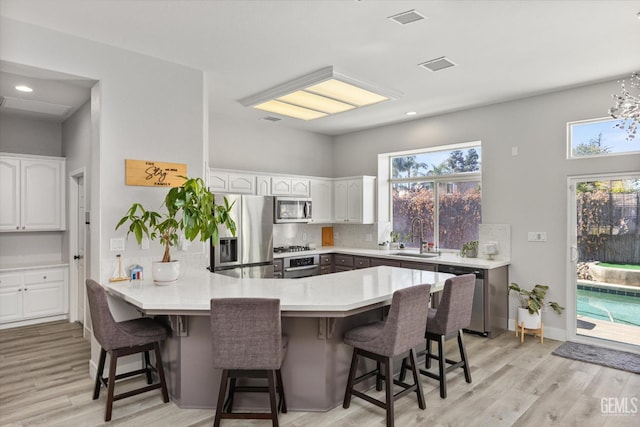 10809 Mirage Dr, Bakersfield, CA 93311 - kitchen with appliances with stainless steel finishes, a peninsula, a kitchen breakfast bar, white cabinets, and light wood-style flooring