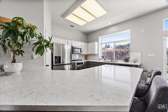 10809 Mirage Dr, Bakersfield, CA 93311 - kitchen with stainless steel appliances, a peninsula, light stone countertops, white cabinets, and a kitchen bar