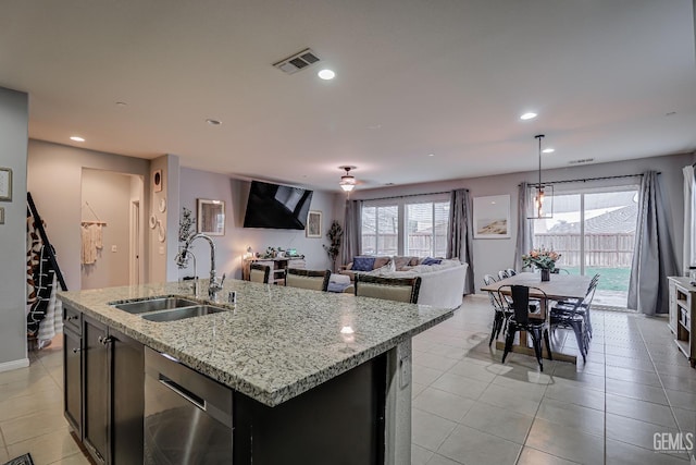 kitchen with sink, a center island with sink, light tile patterned floors, dishwasher, and light stone countertops