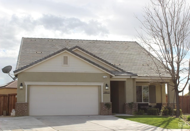 view of front facade featuring stucco siding, fence, concrete driveway, an attached garage, and brick siding