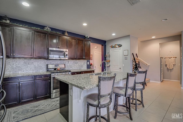 kitchen featuring sink, tasteful backsplash, stainless steel appliances, light stone countertops, and a kitchen island with sink