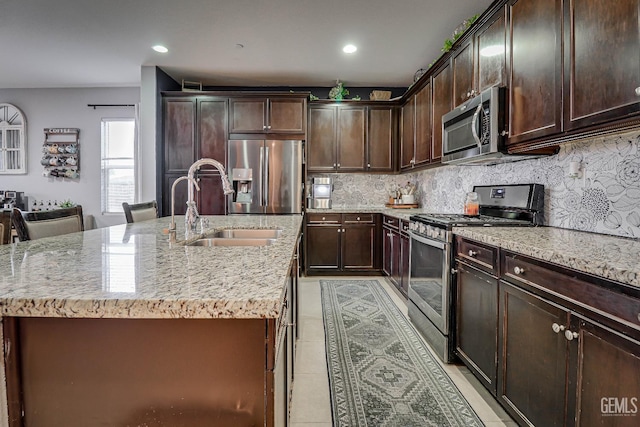 kitchen with dark brown cabinetry, appliances with stainless steel finishes, sink, and a center island with sink