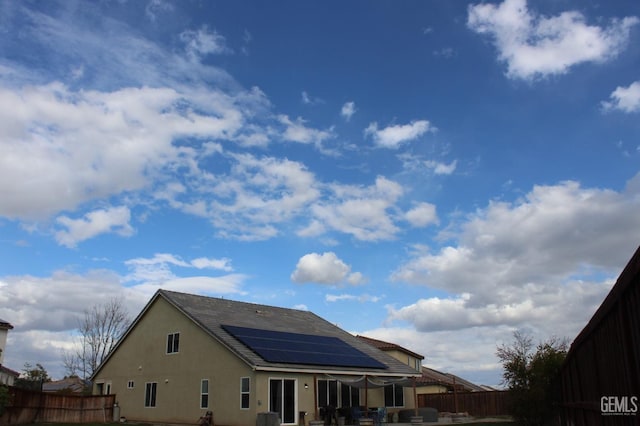 rear view of house featuring stucco siding, solar panels, and a fenced backyard