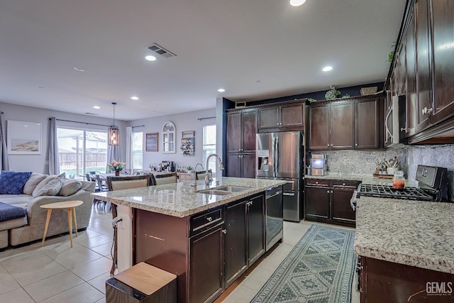 kitchen featuring sink, a kitchen island with sink, light tile patterned floors, stainless steel appliances, and light stone countertops