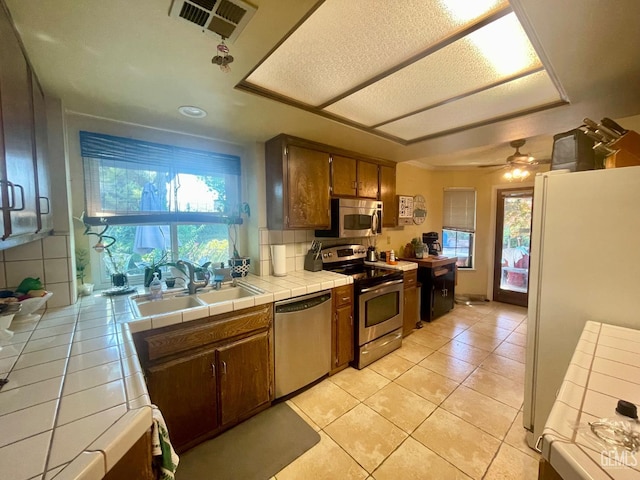 9125 Gleeson Ct, Bakersfield, CA 93311 - kitchen with stainless steel appliances, tile counters, a sink, light tile patterned floors, and a ceiling fan