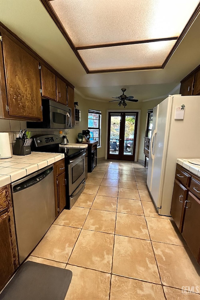 9125 Gleeson Ct, Bakersfield, CA 93311 - kitchen with stainless steel appliances, tile counters, dark brown cabinets, light tile patterned floors, and french doors