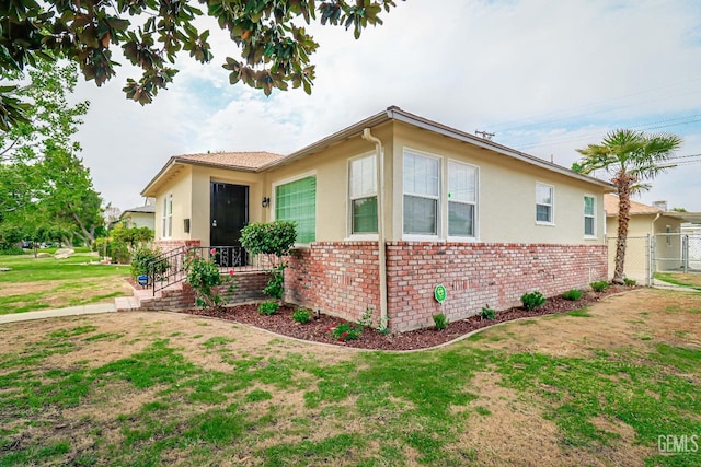 view of front of home featuring stucco siding, a front yard, fence, and brick siding