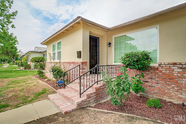 view of exterior entry with brick siding, a yard, and stucco siding