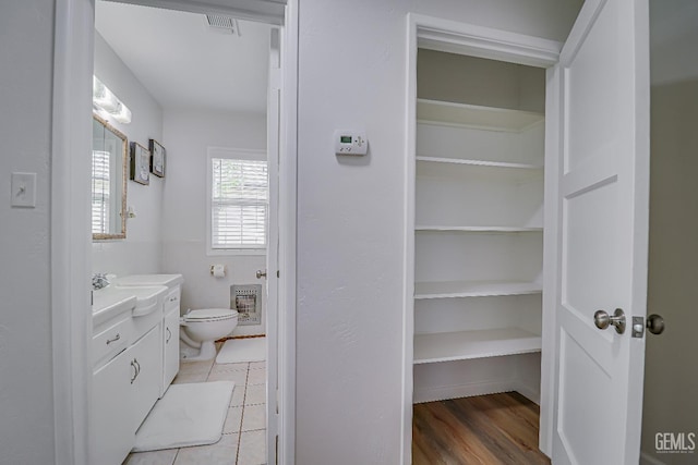 bathroom with toilet, heating unit, a spacious closet, vanity, and tile walls