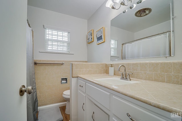 bathroom featuring wainscoting, toilet, tile walls, and vanity