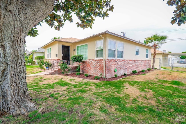 view of front of home with a front yard, brick siding, fence, and stucco siding