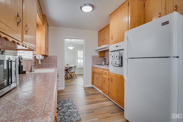 kitchen with light countertops, light wood-style floors, a sink, white appliances, and under cabinet range hood