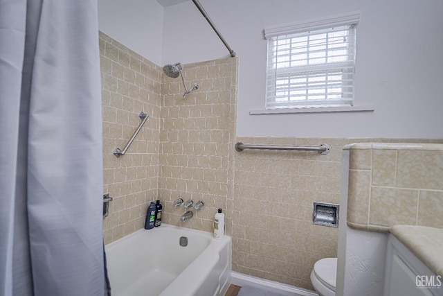 bathroom featuring toilet, tile walls, shower / bath combination with curtain, and wainscoting