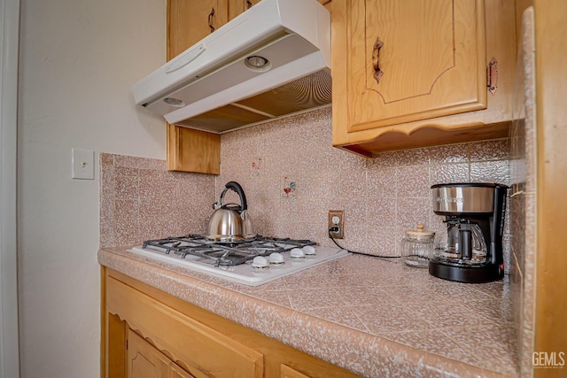 kitchen featuring under cabinet range hood, white gas cooktop, and decorative backsplash