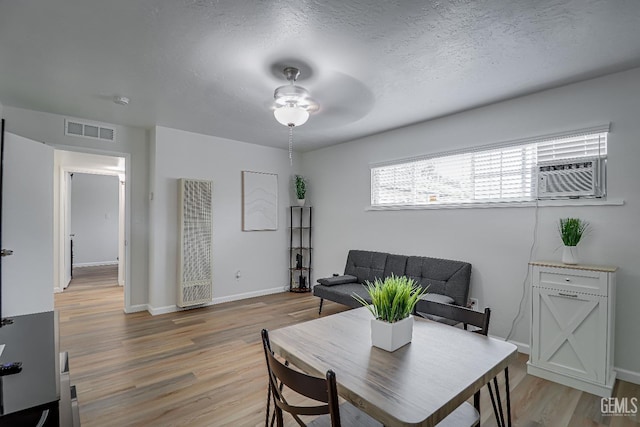 dining area featuring light wood finished floors, baseboards, visible vents, and a textured ceiling